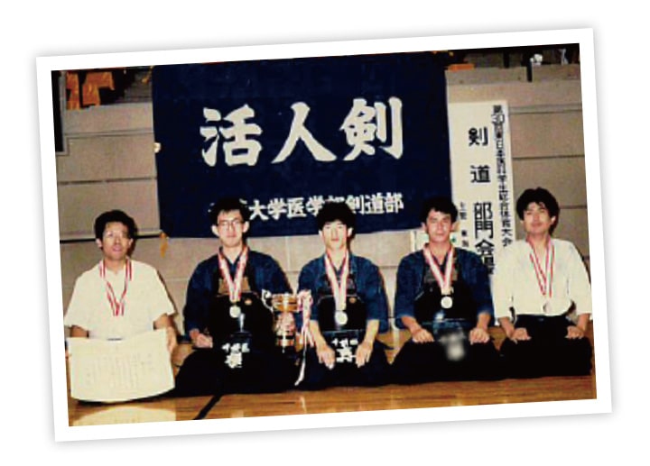 優勝杯を持ち正座で座る大学時代の横手学長と剣道部の仲間